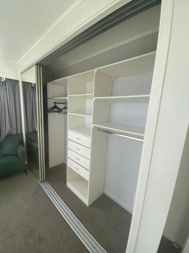 a closet with white shelves and a blue chair at Spacious Sunny Room in Auckland