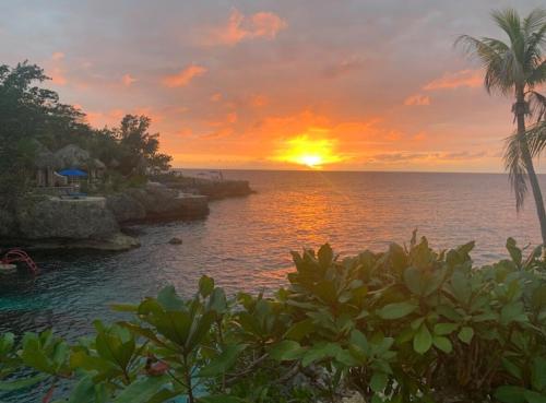 a sunset over the ocean with a pool and palm trees at Whitehall Villa in Negril in Negril