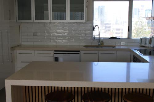 cocina con armarios blancos y barra con taburetes en Marriner Views, en Gold Coast