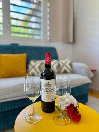 a bottle of wine and two wine glasses on a table at Le Cocon Miel - Plage, Jardin, Adapté aux Groupes in Folle Anse