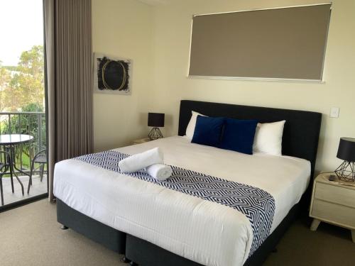 a bedroom with a bed with blue pillows and a balcony at Meridian Alex Beach Apartments in Alexandra Headland