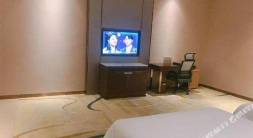 a room with a television and a desk with a chair at Venus Royal Hotel Nanning East High-Speed Railway Station in Nanning