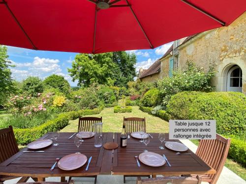 une table en bois avec un parasol rouge dans un jardin dans l'établissement La Breteche du Perche, à Saint-Germain-de-la-Coudre