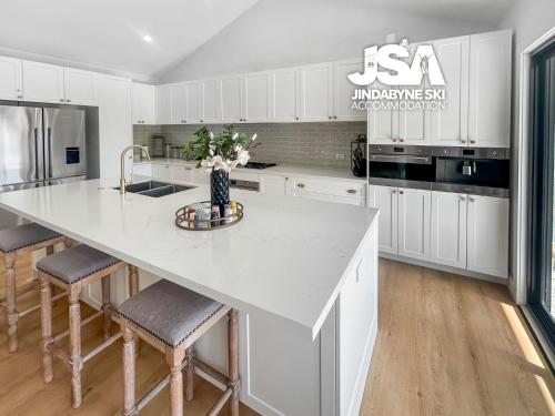 a kitchen with white cabinets and a large island with stools at Allenvale in Jindabyne
