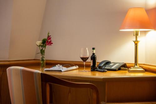 a desk with a lamp a phone and a glass of wine at Waldhaus Reinbek in Reinbek