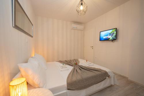 a bedroom with a white bed and a tv on the wall at Pool and Breakfast Apartments Villa Maro in Novalja