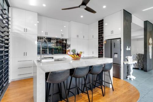 a kitchen with white cabinets and a counter with bar stools at Belle Escapes Villa Riviera in Palm Cove