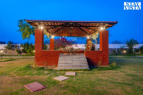 a brick pergola with a table and chairs under it at StayVista at The Mira House with Pool, WiFi in Sohna