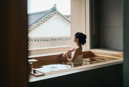 a woman sitting in a bathtub in front of a window at IJE Gyeongju in Gyeongju