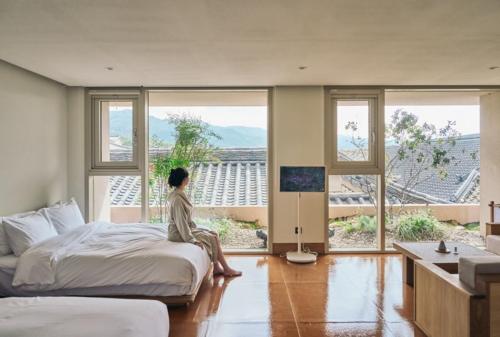 a woman sitting on a bed in a room with windows at IJE Gyeongju in Gyeongju