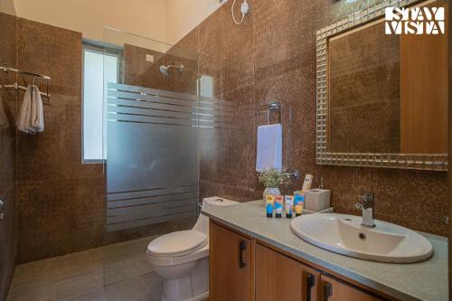 a bathroom with a sink and a toilet and a mirror at StayVista at Echoes of Ease with Bonfire & WiFi in Rishīkesh