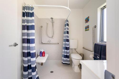 a bathroom with a shower curtain and a toilet at Kombi Cottage Fully accessible in Tairua