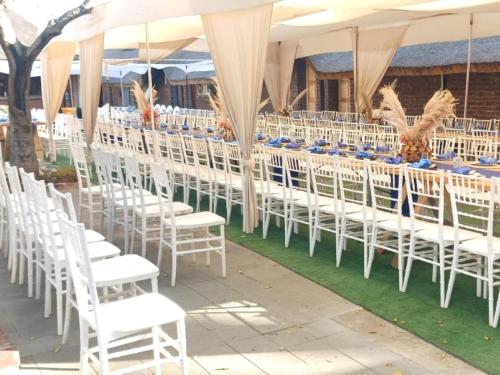 una fila de sillas y mesas blancas en una carpa en Bostons Lodge & Restaurant, en Jan Kempdorp