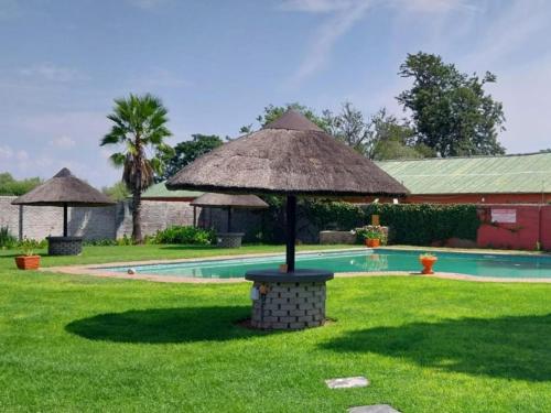 una sombrilla en el césped junto a una piscina en Bostons Lodge & Restaurant, en Jan Kempdorp