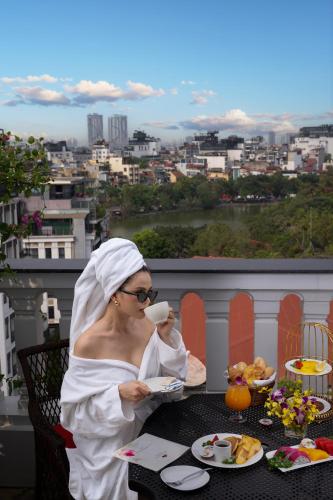 a woman sitting at a table with a cup of coffee at The Oriental Jade Hotel in Hanoi