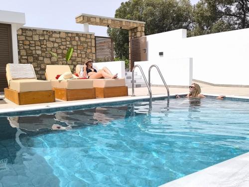 two women laying on chairs in a swimming pool at Valantina's & Mannouel Lardos Luxury Villas in Lardos