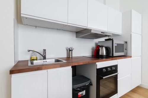 une cuisine blanche avec un évier et un micro-ondes dans l'établissement Appartement cosy refait a neuf - Paris 19 - 4P, à Paris