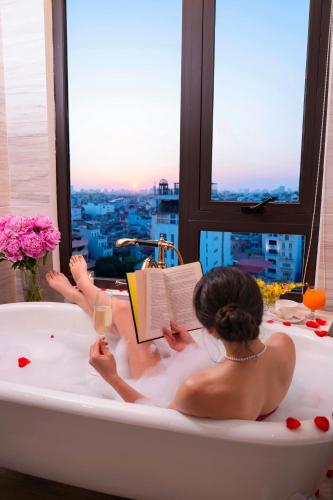 a woman laying in a bath tub reading a book at The Oriental Jade Hotel in Hanoi