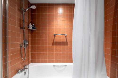 a bathroom with a tub and a shower with a shower curtain at Crown Hotel in Chertsey