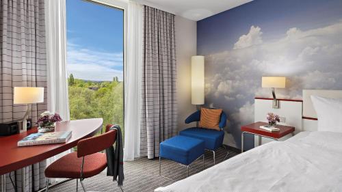a hotel room with a bed and a desk and a window at Hey Lou Hotel Friedrichshafen in Friedrichshafen