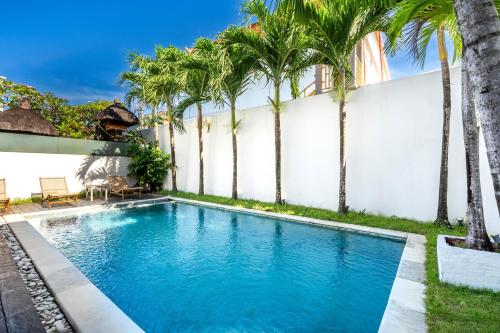 einen Pool mit Palmen vor einer weißen Wand in der Unterkunft Villa Oberoi in Seminyak