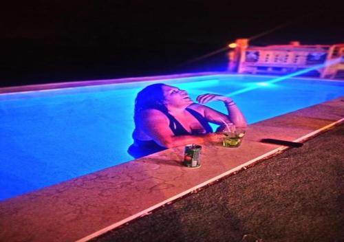 a woman sitting next to a swimming pool with drinks at Fenti Nubian Resort in Aswan