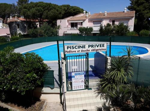 une clôture avec un panneau en face d'une piscine dans l'établissement La Casa Soléa appartement pinède T2 résidence Eureka à 5min à pied du village naturiste, au Cap d'Agde