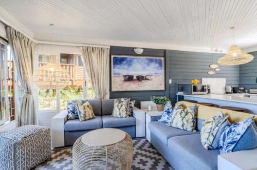 a living room with blue couches and a kitchen at Knysna River Club Getaways - Luxury waterfront chalets in Knysna
