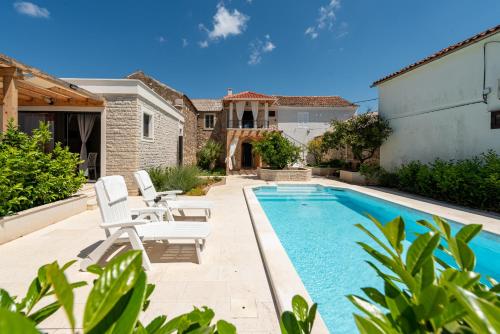 a backyard with a swimming pool and two white chairs at Apartment Varos with shared pool in Ugljan