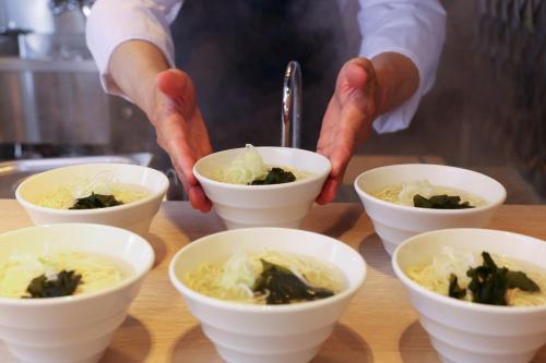 a chef preparing food in white bowls on a table at KAMENOI HOTEL Kujukuri in Asahi