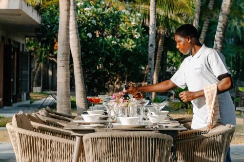 un homme debout devant une table avec des assiettes dans l'établissement Maya kobe Beachfront Retreat Kilifi, à Kilifi