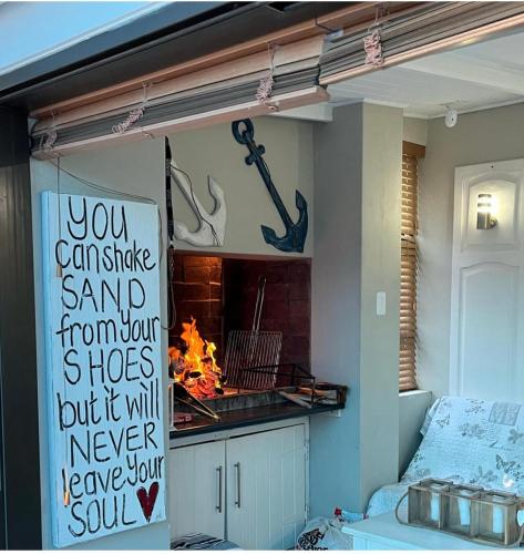 a kitchen with a fireplace and a sign that says you can shake sand from your at Huisie by die See in Stilbaai