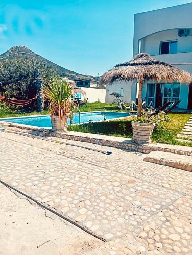 a resort with a swimming pool and a straw umbrella at VILLA SOUNINE RAFRAF avec piscine in Bizerte