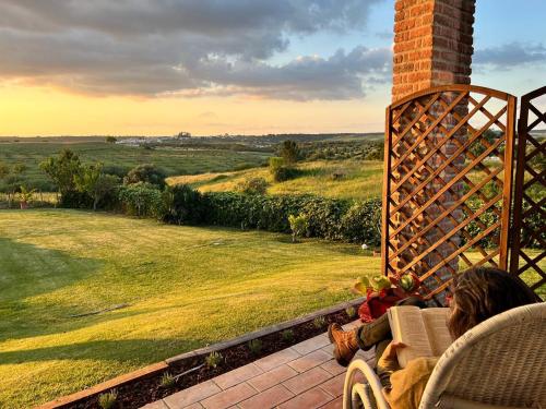 a woman sitting on a porch looking out at a field at Courela da Azinheira - Country Guesthouse in Lavre