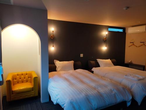 a hotel room with two beds and a yellow chair at Hotel Unica in Biei