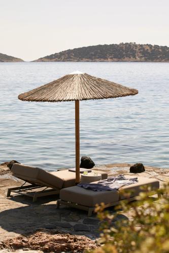 two lounge chairs under an umbrella on the beach at Minos Beach Art Hotel, a Member of Design Hotels in Agios Nikolaos