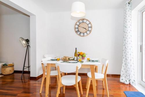 a dining room table with white chairs and a clock on the wall at GuestReady - Monaco Nest in Ponta Delgada