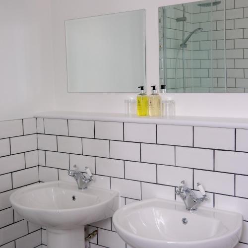 a white bathroom with two sinks and a mirror at Glen Mhor Hotel at Uile-bheist 'Brewstillery' in Inverness