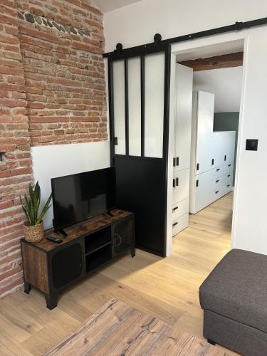 un salon avec une télévision et un mur en briques dans l'établissement T2 de charme, au cœur de ville avec climatisation, à Toulouse