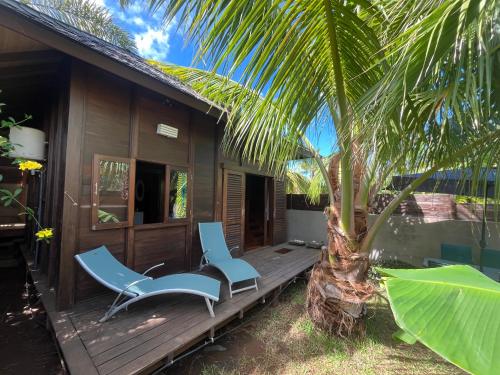 a porch of a house with two chairs and a palm tree at Chalet Bali, avec SPA et proche lagon in Saint-Gilles les Bains