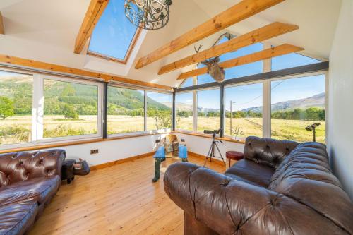 ein Wohnzimmer mit einem Ledersofa und großen Fenstern in der Unterkunft Meadow View in Lochearnhead