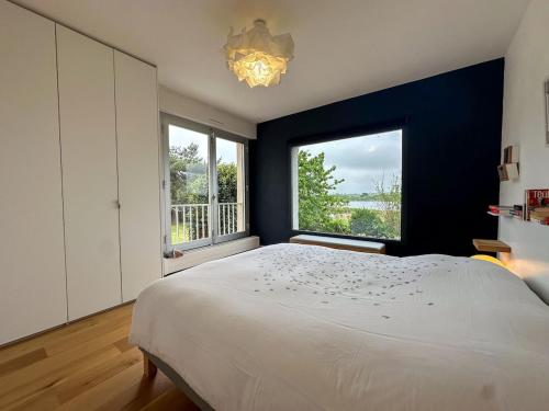 une chambre avec un grand lit et deux fenêtres dans l'établissement Maison spacieuse et élégante vue sur l'etang de Lannenec à 600m du Fort-Bloqué, à Ploemeur