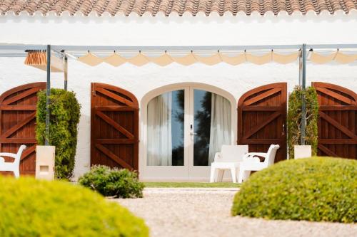 a white house with wooden doors and white chairs at Hotel Rural Binigaus Vell in Es Migjorn Gran