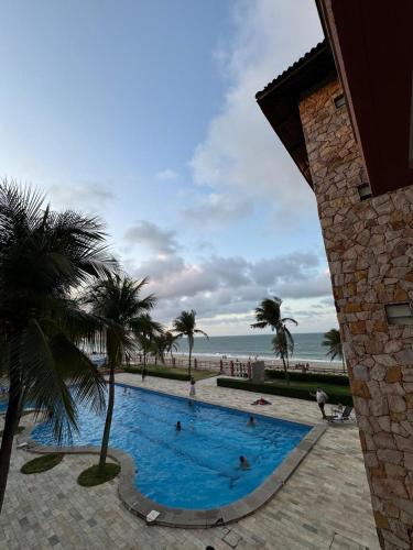 a swimming pool next to a beach with palm trees at Kariri Beach Residence in Caucaia