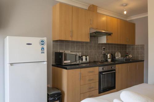 a kitchen with wooden cabinets and a white refrigerator at Kingfisher Court Apartments by UNO in Slough