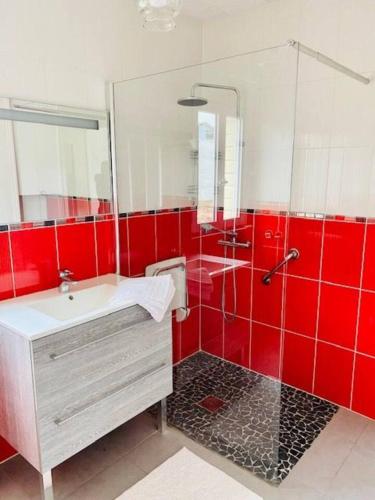 La salle de bains rouge est pourvue d'un lavabo et d'une douche. dans l'établissement Gite de Coquelicots avec Jacuzzi à Embreville, à Embreville