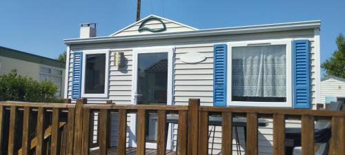 une maison avec des fenêtres bleues et blanches et une clôture dans l'établissement Camping du Gouffre - Mobil-home 082, à Plougrescant