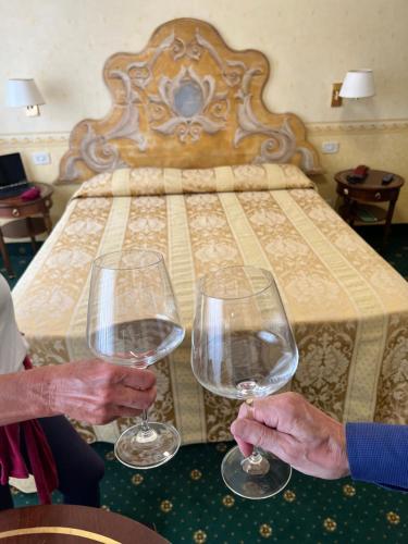 two people holding wine glasses in front of a bed at Hotel Alla Riviera in Bardolino