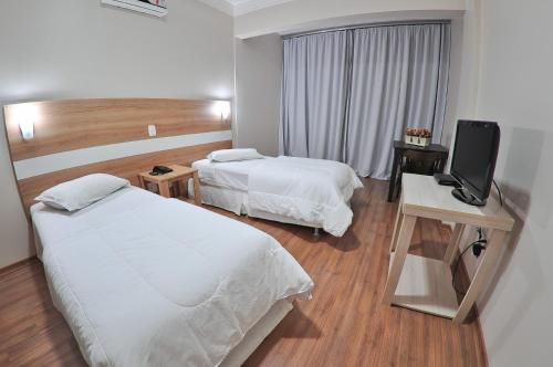 a hotel room with two beds and a flat screen tv at Turis Hotel in Passo Fundo