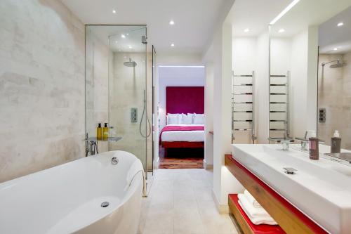 a white bathroom with a tub and a bedroom at Residences at The Gyle - London in London